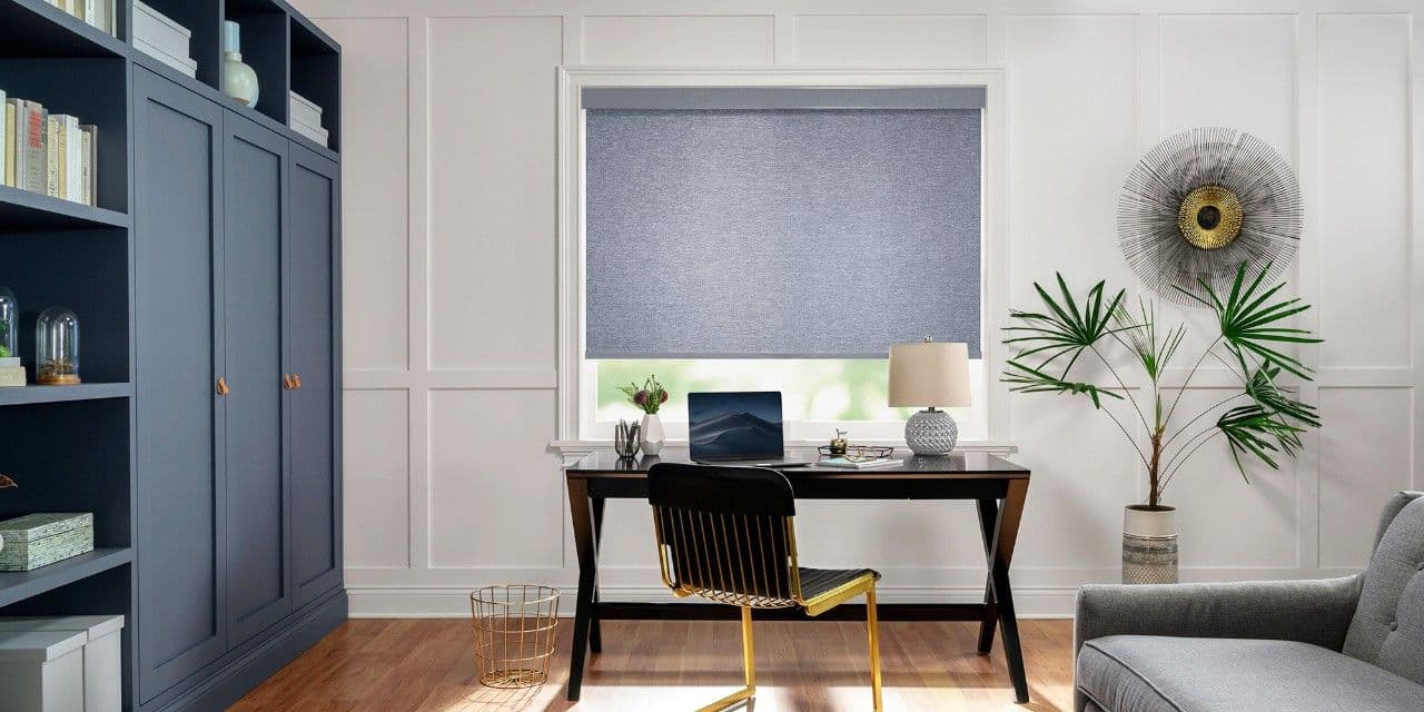 Grey roller shade above a desk in a home office with navy cabinetry